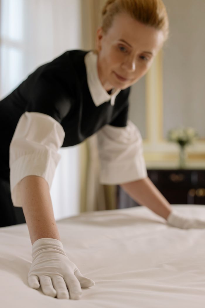 journey A housekeeper elegantly arranges bed sheets in a luxurious hotel room, showcasing hospitality expertise.