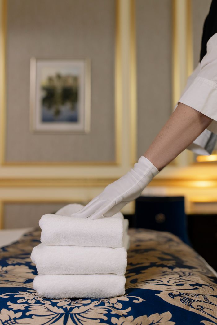 services-04 A hotel housekeeper in uniform arranges freshly laundered towels in a luxurious room.